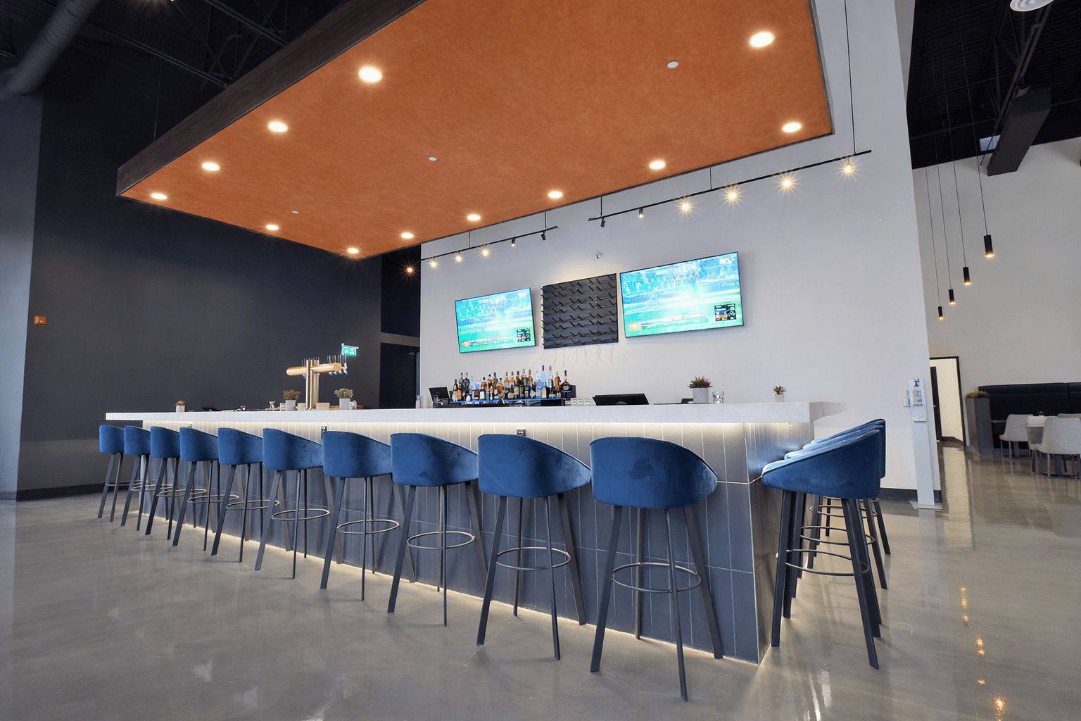 Custom commercial bar construction with quartz countertop, blue upholstered bar stools, integrated lighting, and premium finishes in Toronto
