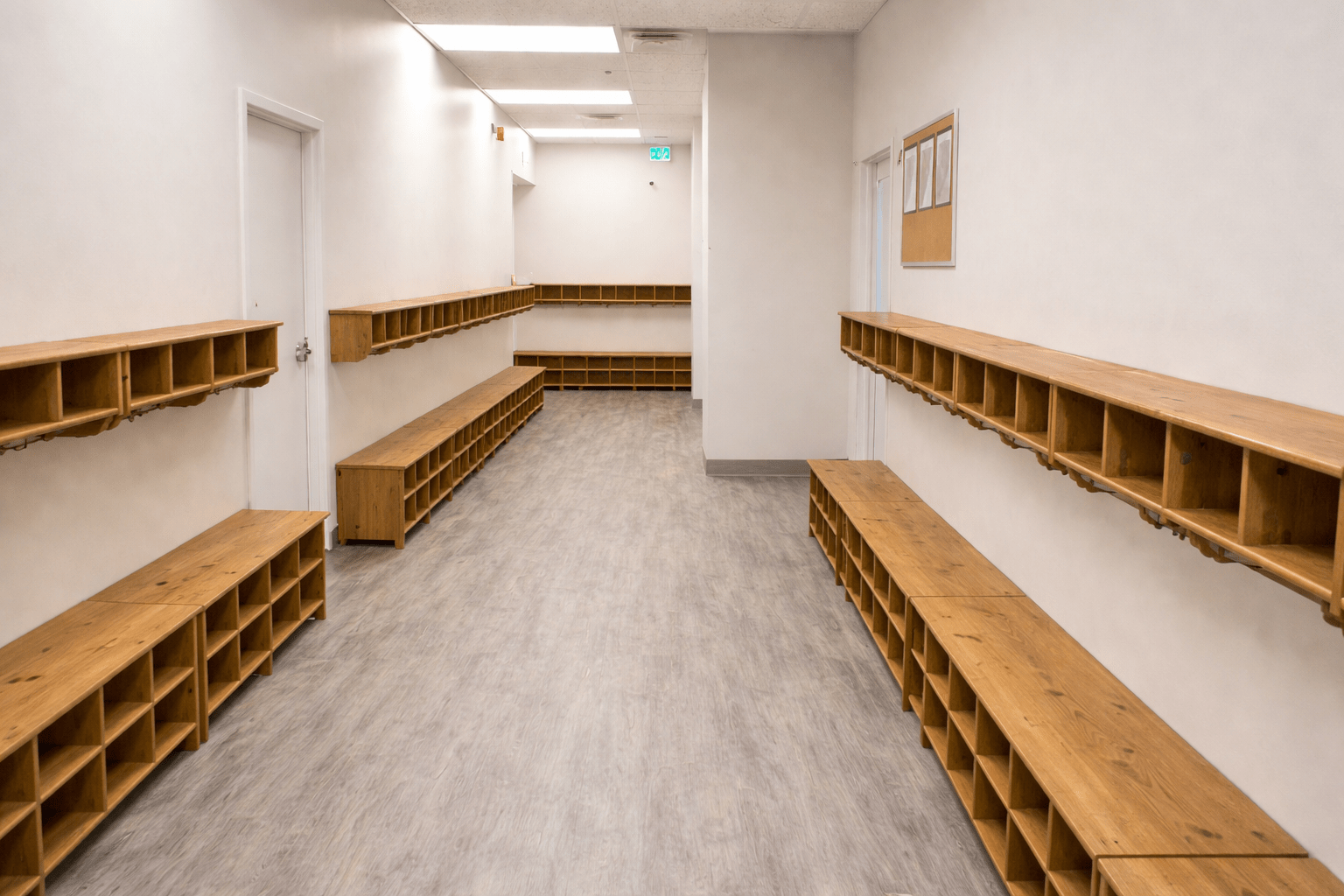 Daycare cubby storage hallway with custom wood millwork benches, integrated coat hooks, durable vinyl flooring, and code-compliant circulation space for childcare facility