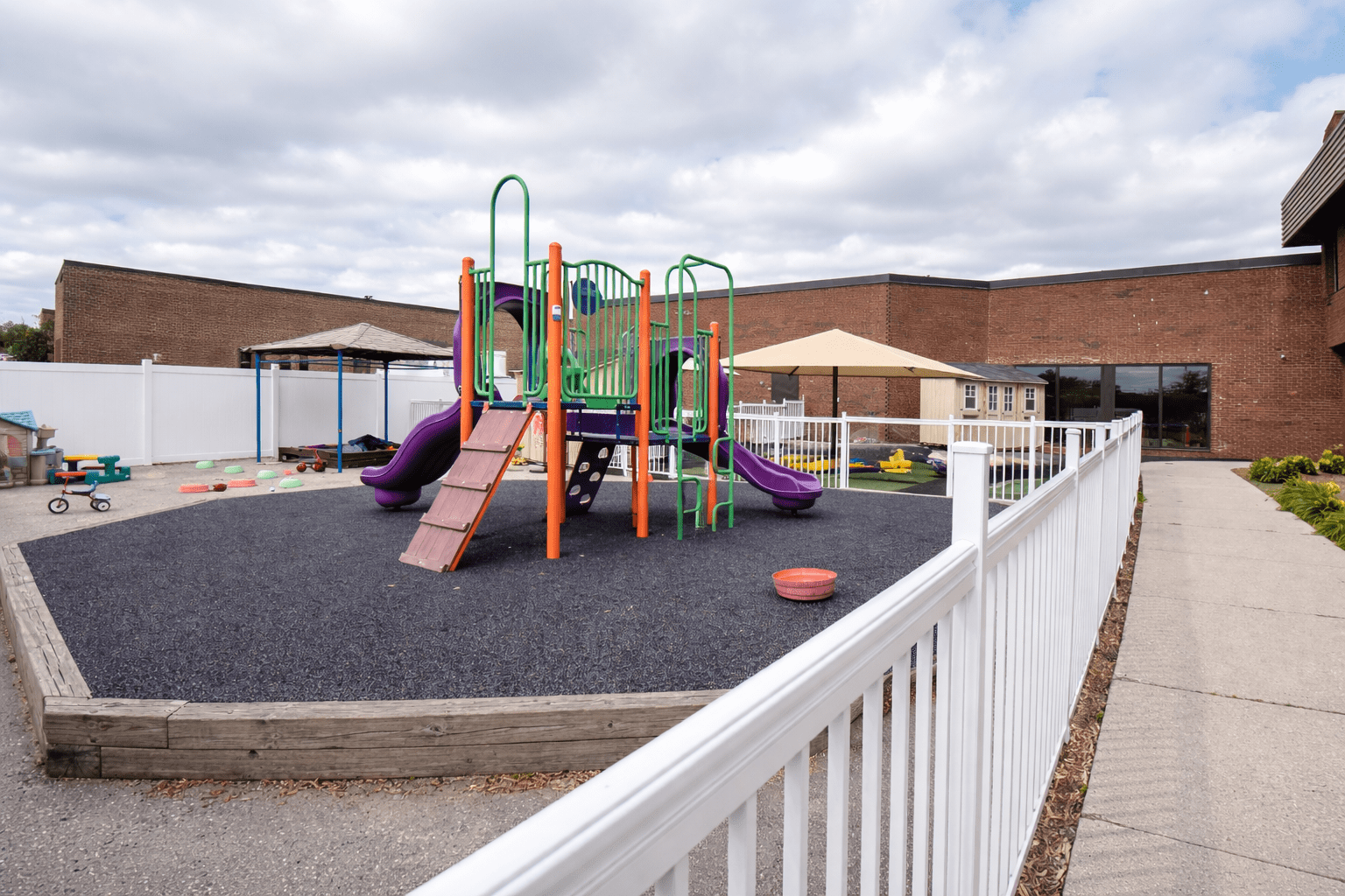 Commercial daycare outdoor playground with rubber safety surfacing, fenced perimeter, play structures, and compliant site design for licensed childcare facility