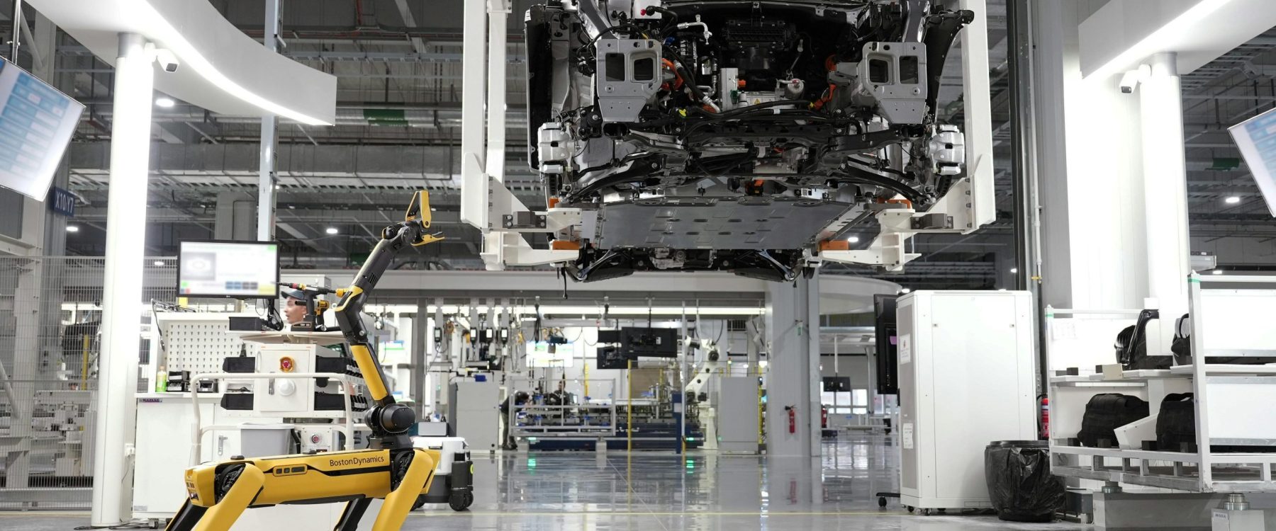 A robotic dog oversees an automated car assembly in a high-tech factory setting.