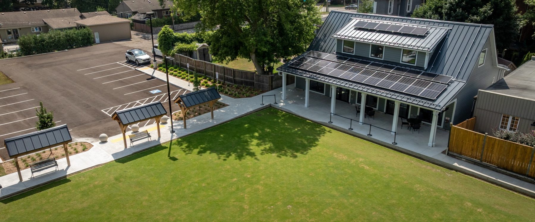 Wilkin Family Community Centre in Paris, Ontario, constructed by GTA General Contractors. The modern net-zero building features solar panels on a pitched roof, a covered patio with seating, landscaped parking, and a large green lawn, blending sustainability with community use.