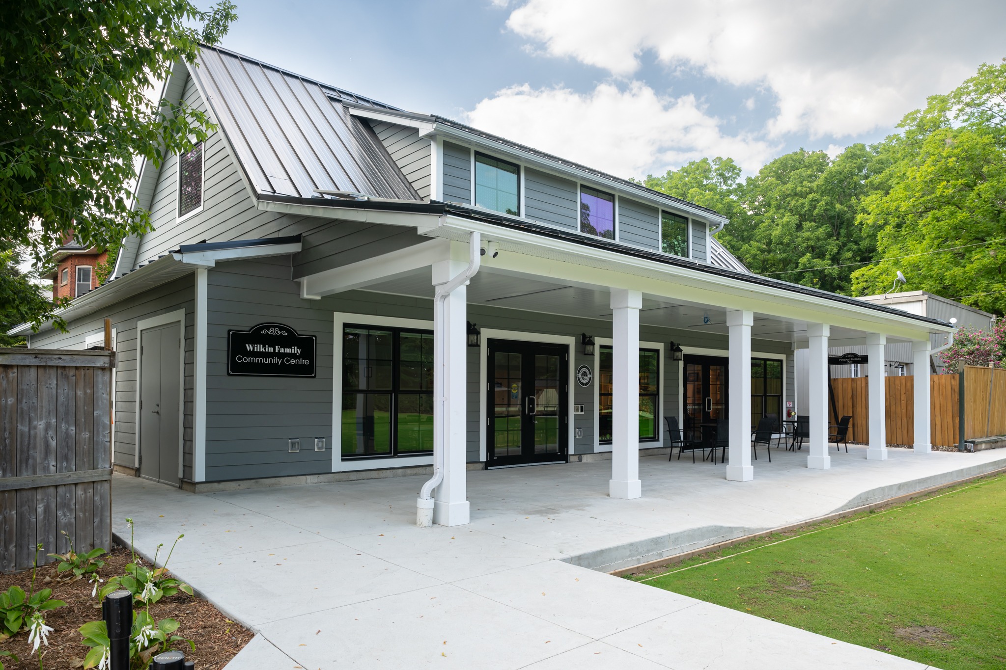 Wilkin Family Community Centre in Paris, Ontario, constructed by GTA General Contractors. The modern net-zero building features solar panels on a pitched roof, a covered patio with seating, landscaped parking, and a large green lawn, blending sustainability with community use.