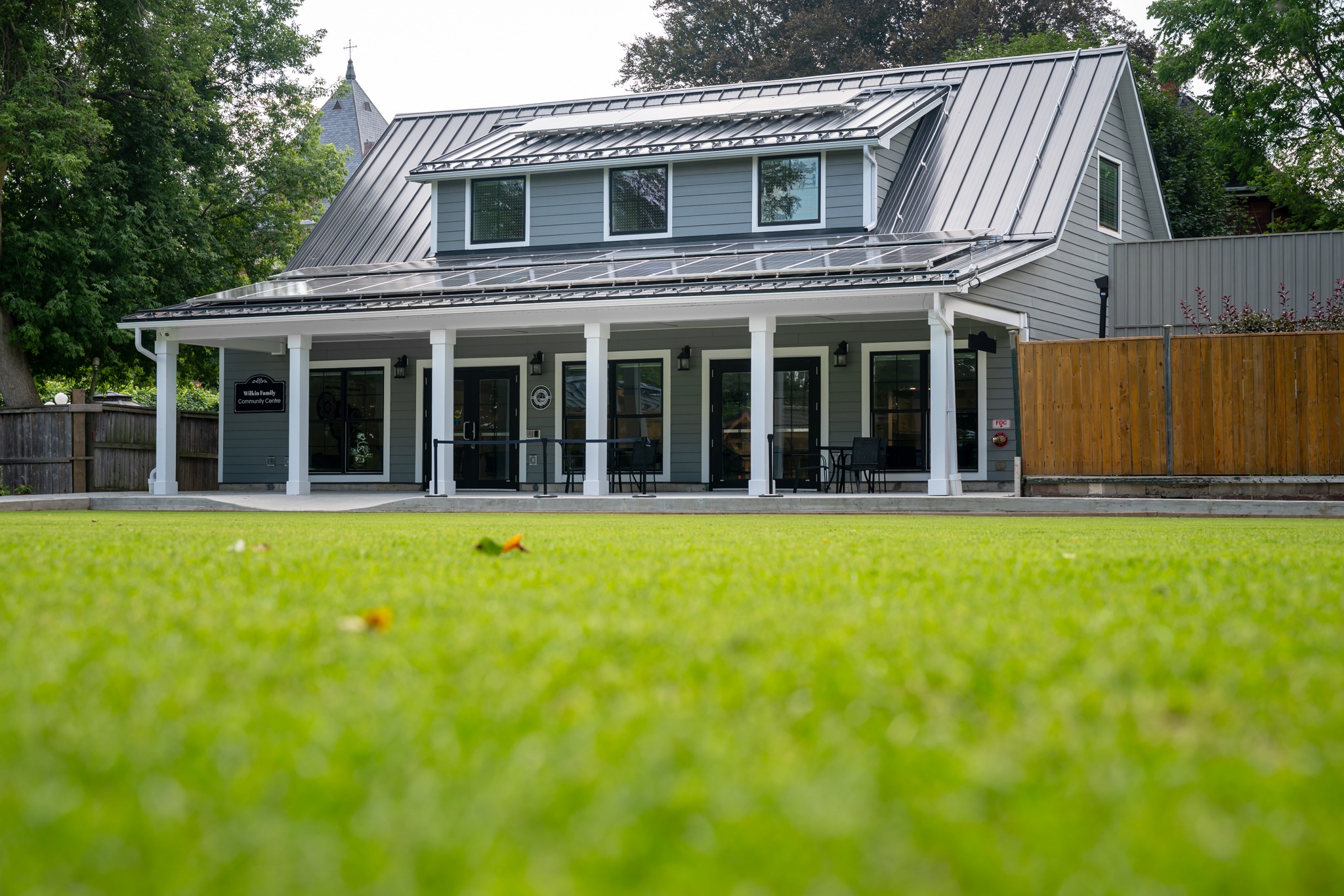 Wilkin Family Community Centre in Paris, Ontario, constructed by GTA General Contractors. The modern net-zero building features solar panels on a pitched roof, a covered patio with seating, landscaped parking, and a large green lawn, blending sustainability with community use.