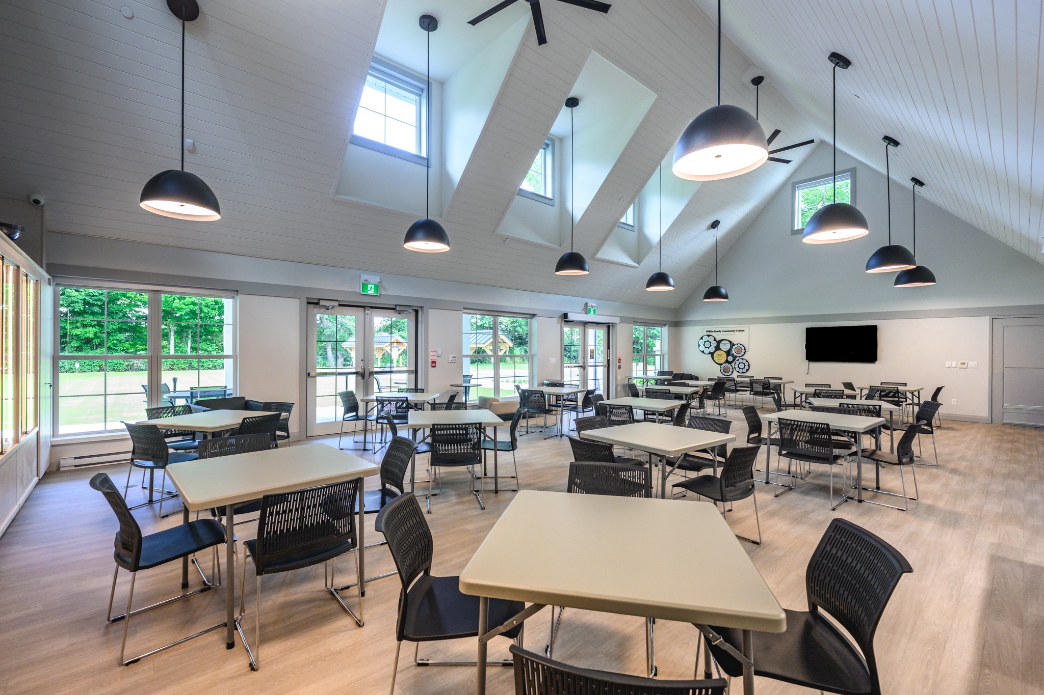 Wilkin Family Community Centre in Paris, Ontario, constructed by GTA General Contractors. The modern net-zero building features solar panels on a pitched roof, a covered patio with seating, landscaped parking, and a large green lawn, blending sustainability with community use.