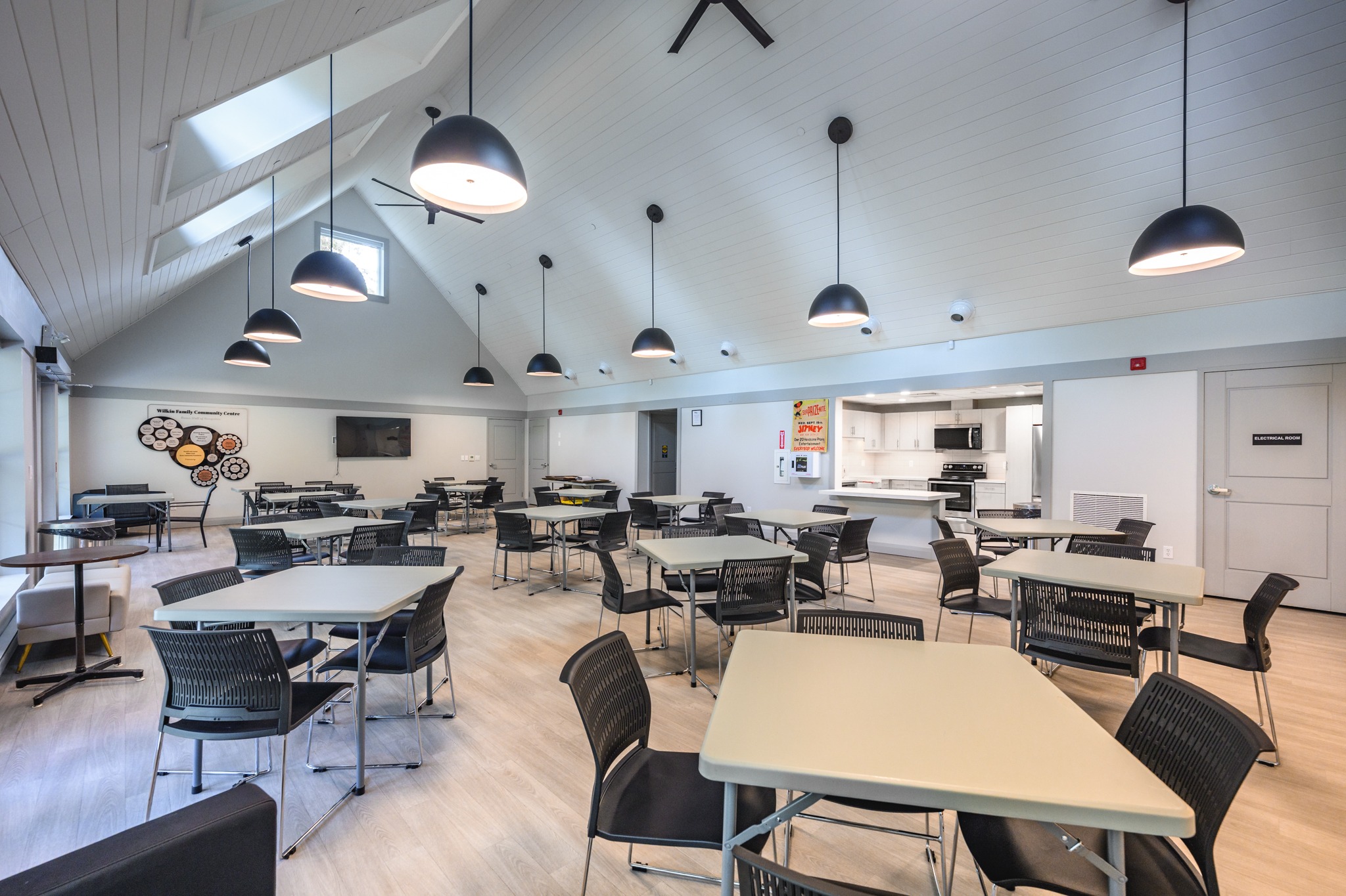 Wilkin Family Community Centre in Paris, Ontario, constructed by GTA General Contractors. The modern net-zero building features solar panels on a pitched roof, a covered patio with seating, landscaped parking, and a large green lawn, blending sustainability with community use.