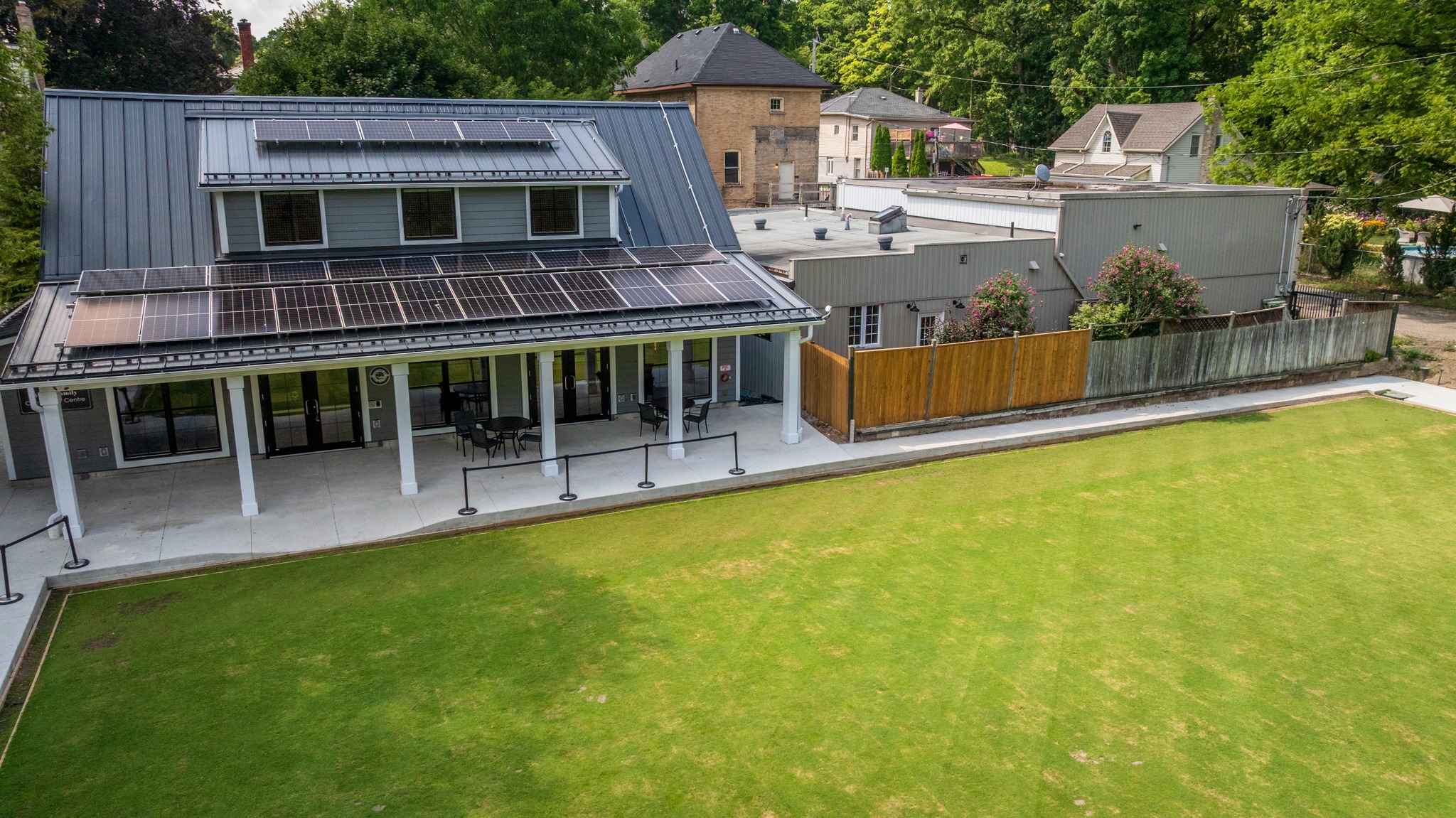 Wilkin Family Community Centre in Paris, Ontario, constructed by GTA General Contractors. The modern net-zero building features solar panels on a pitched roof, a covered patio with seating, landscaped parking, and a large green lawn, blending sustainability with community use.