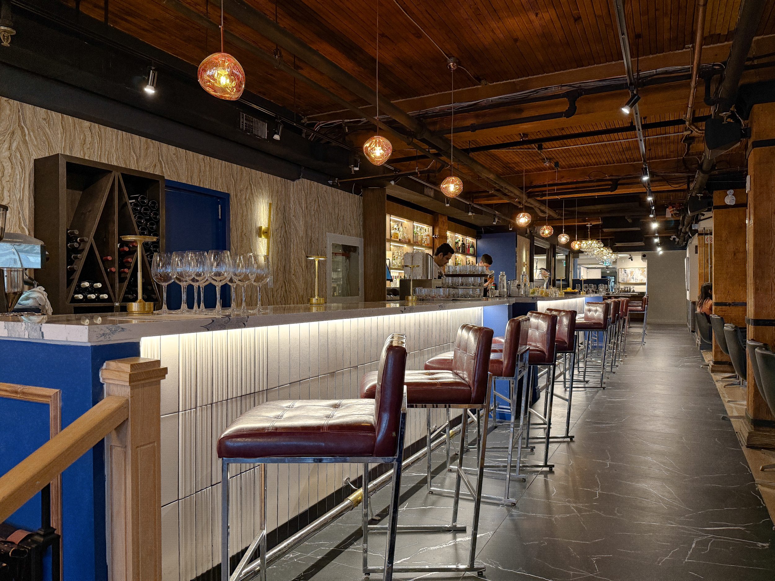 Custom bar and entry area at BLU Ristorante on King Street West, Toronto, featuring marble-look flooring, blue millwork, brass accents, and warm decorative lighting.