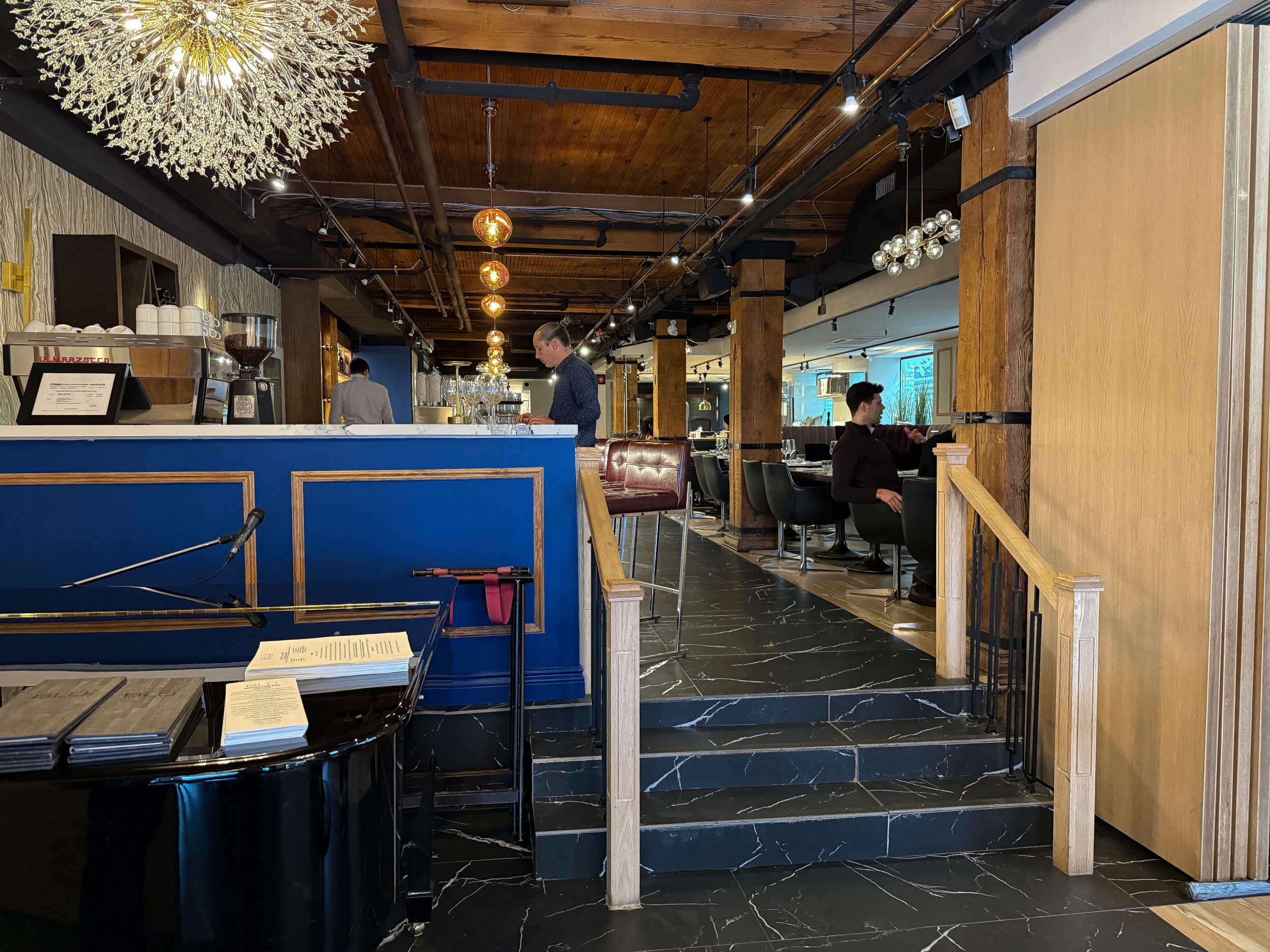 Entry area at BLU Ristorante on King Street West, Toronto, featuring marble-look flooring, blue millwork, brass accents, and warm decorative lighting.