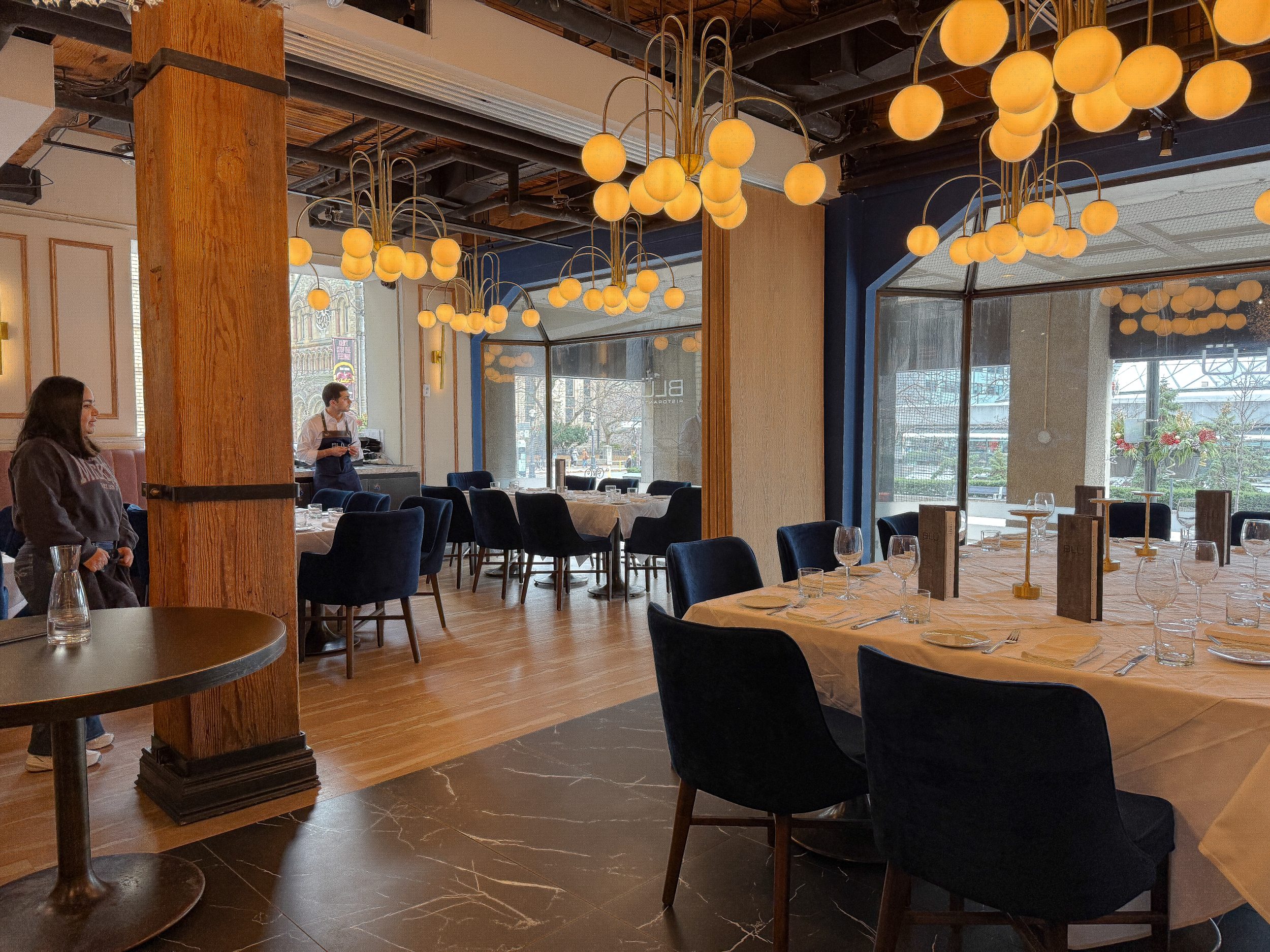 Main dining room at BLU Ristorante Toronto showcasing custom chandeliers, wood columns, upholstered seating, and an elegant open dining layout.