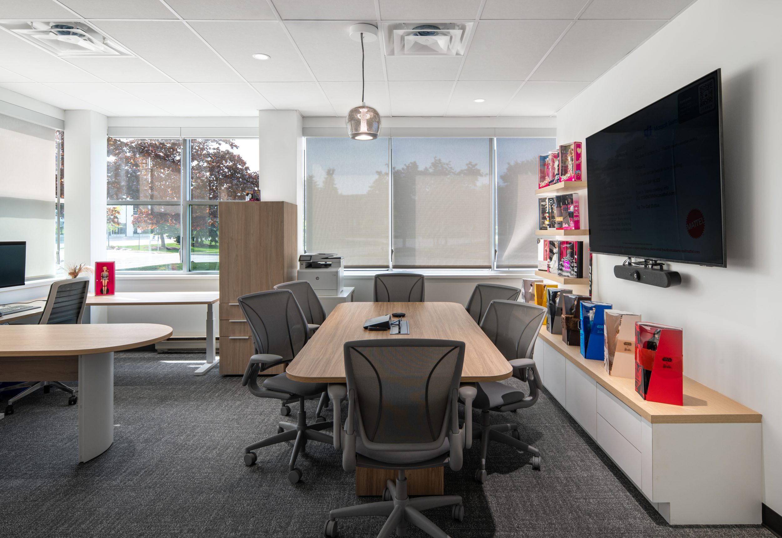 Executive office and private meeting space at Mattel Canada Headquarters in Mississauga, Ontario, featuring a custom wood conference table, integrated audiovisual technology, built-in display cabinetry, ergonomic office furniture, natural light, product displays, and modern corporate office interiors delivered through a Design-Build renovation.