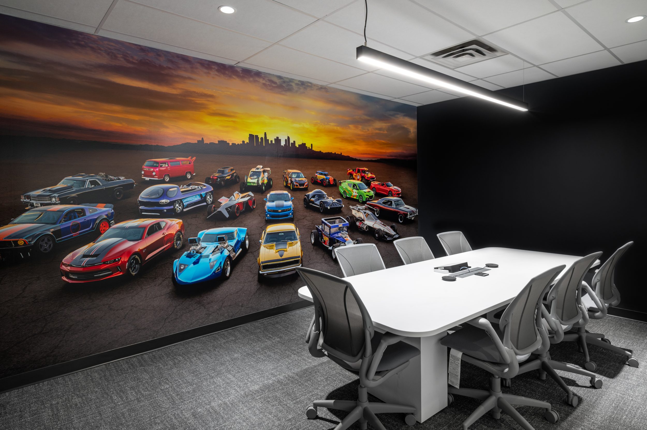 Hot Wheels themed conference room at Mattel Canada Headquarters in Mississauga, Ontario, featuring a custom automotive wall mural, modern conference table, ergonomic meeting chairs, integrated technology, suspended architectural lighting, branded workplace design, and commercial office renovation completed through a Design-Build delivery model.