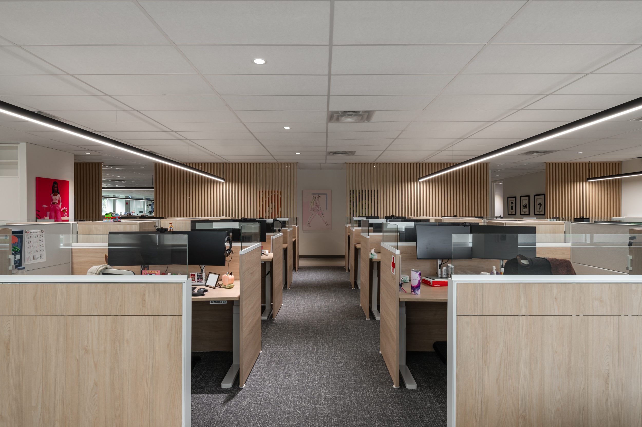 Modern corporate workspace at Mattel Canada Headquarters in Mississauga, Ontario, featuring collaborative workstations, custom millwork partitions, suspended linear lighting, ergonomic seating, integrated computer stations, open office planning, and contemporary commercial interior construction completed through a Design-Build renovation.