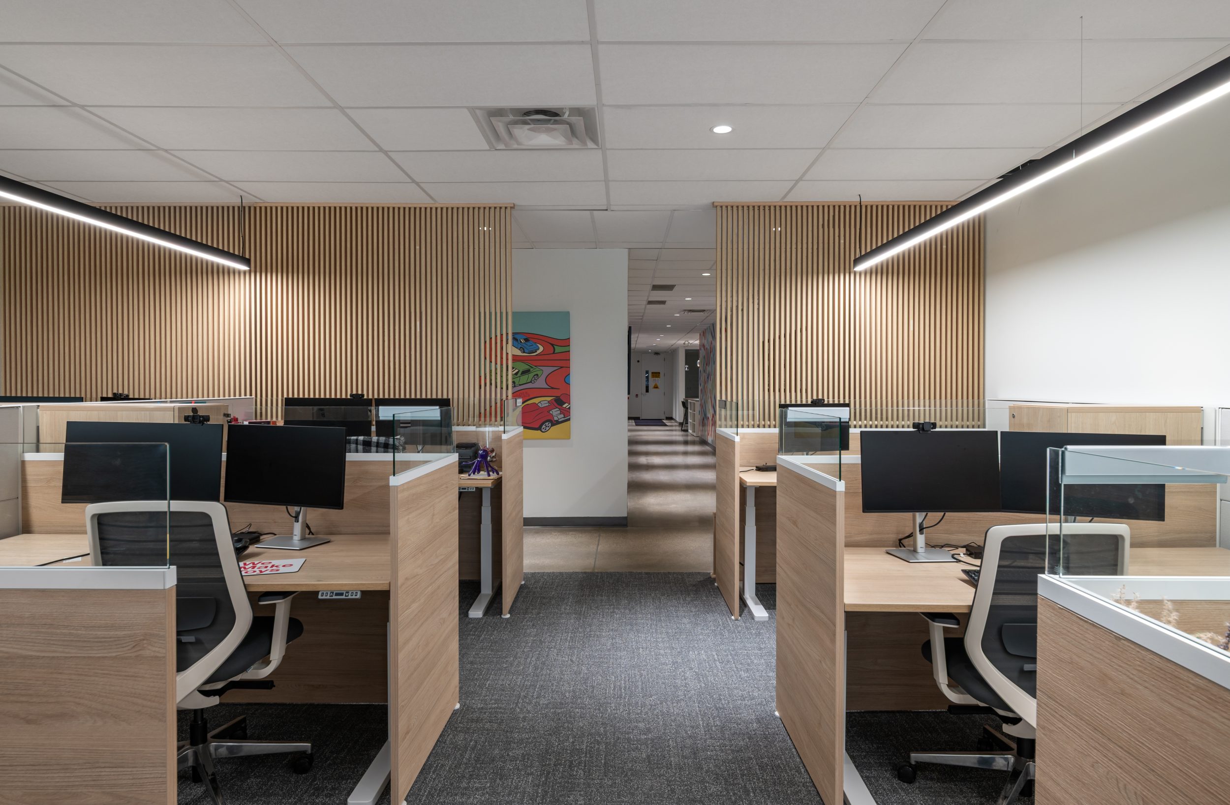 Open-concept corporate workspace at Mattel Canada Headquarters in Mississauga, Ontario, featuring ergonomic office workstations, custom wood slat feature walls, integrated task lighting, glass workstation screens, commercial carpeting, modern workplace planning, and Design-Build office renovation.