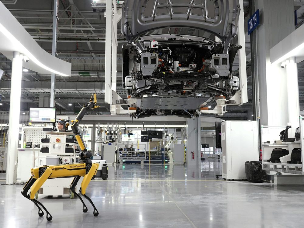 A robotic dog oversees an automated car assembly in a high-tech factory setting.